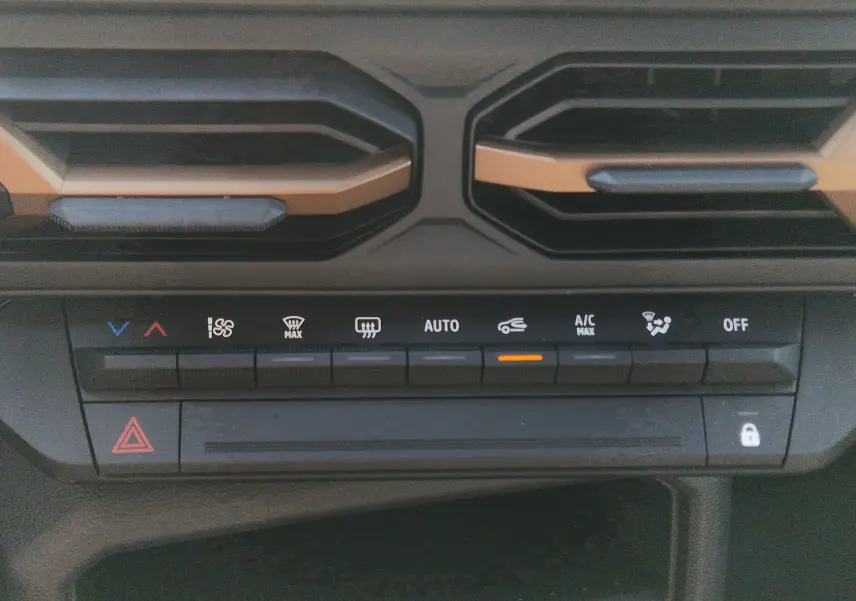 Détail de la console de climatisation du Dacia Duster blanc 2026, avec boutons tactiles et aérateurs noirs et bronze.