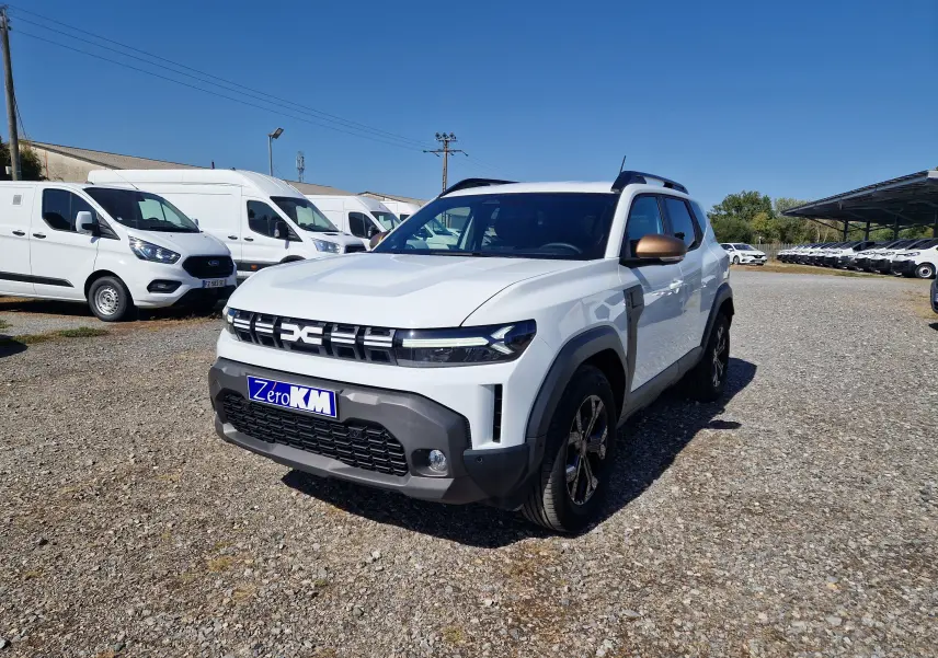 Vue 3/4 avant droite du Dacia Duster blanc 2026 avec rétroviseurs bronze et calandre noire distinctive.