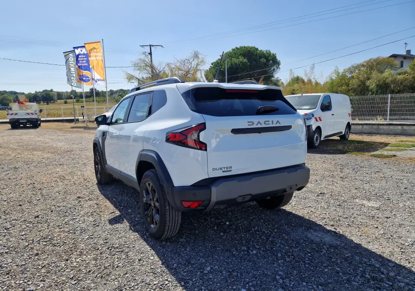 Vue 3/4 arrière droite du Dacia Duster blanc 2026 hybride, avec jantes noires et barres de toit visibles.