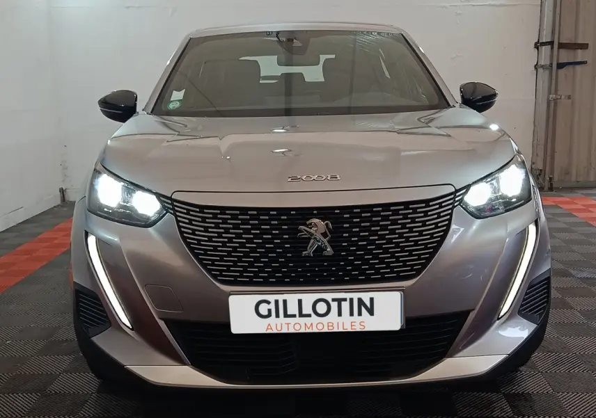 Vue frontale d'un Peugeot E-2008 électrique gris clair avec phares LED allumés et calandre noire distinctive.