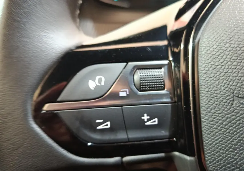Gros plan sur les commandes de volume et de fonction vocale au volant cuir noir d'une Peugeot E-2008 électrique 2023.