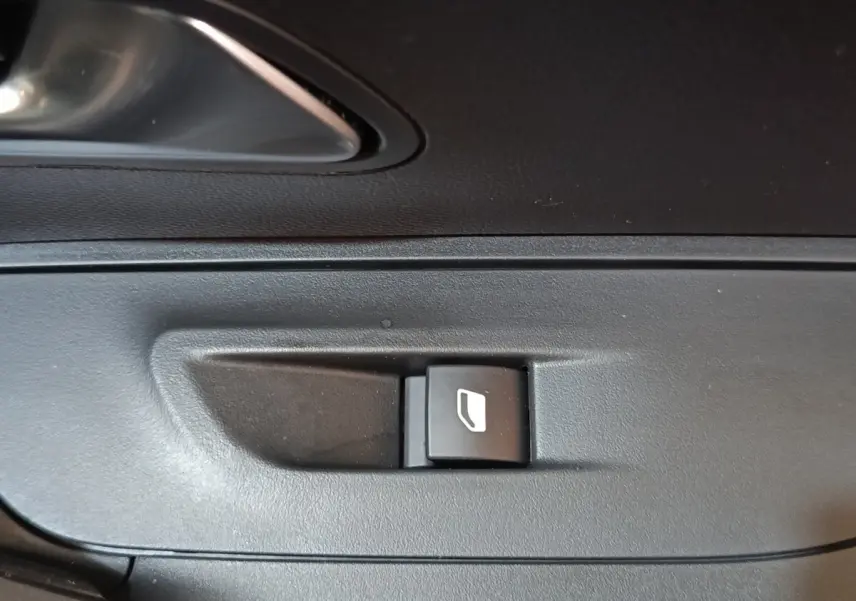 Gros plan sur le bouton de commande de lève-vitre côté conducteur de la Peugeot E-2008 électrique gris clair 2023.