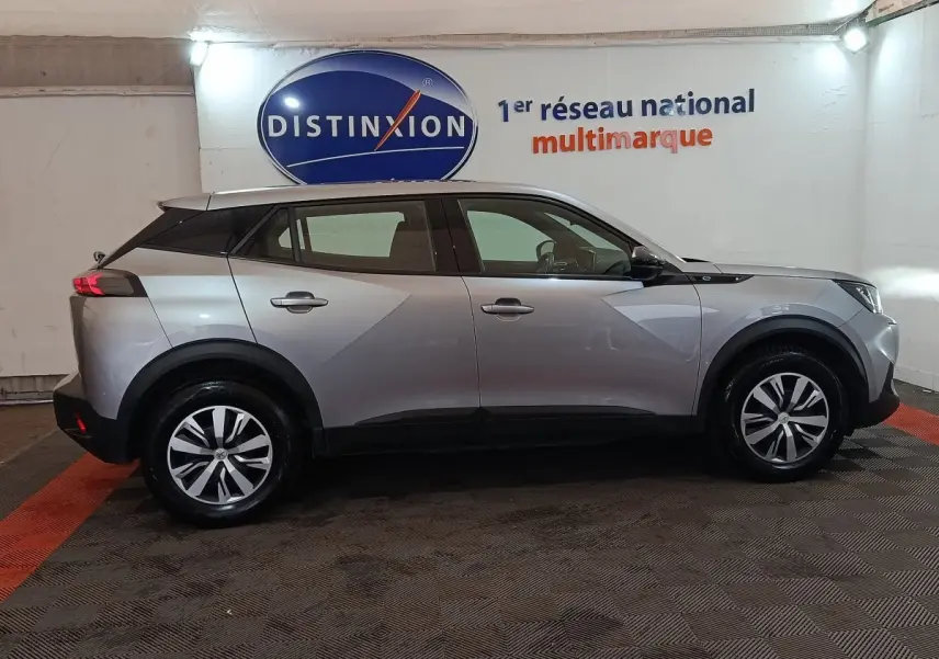 Profil droit d'un Peugeot E-2008 électrique gris clair 2023 avec jantes alliage et toit noir contrasté.