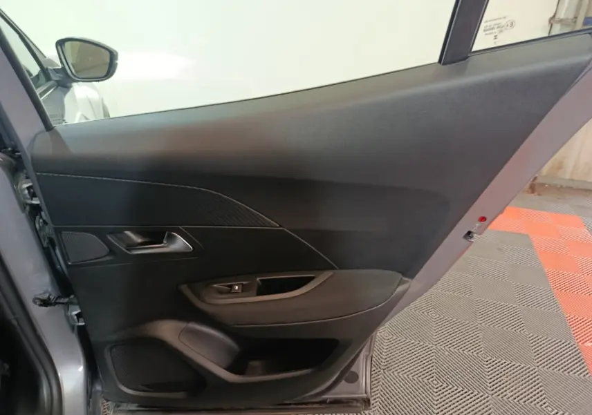 Vue intérieure de la porte arrière gauche gris clair du Peugeot E-2008 électrique 2023, avec poignée et commande de vitre.