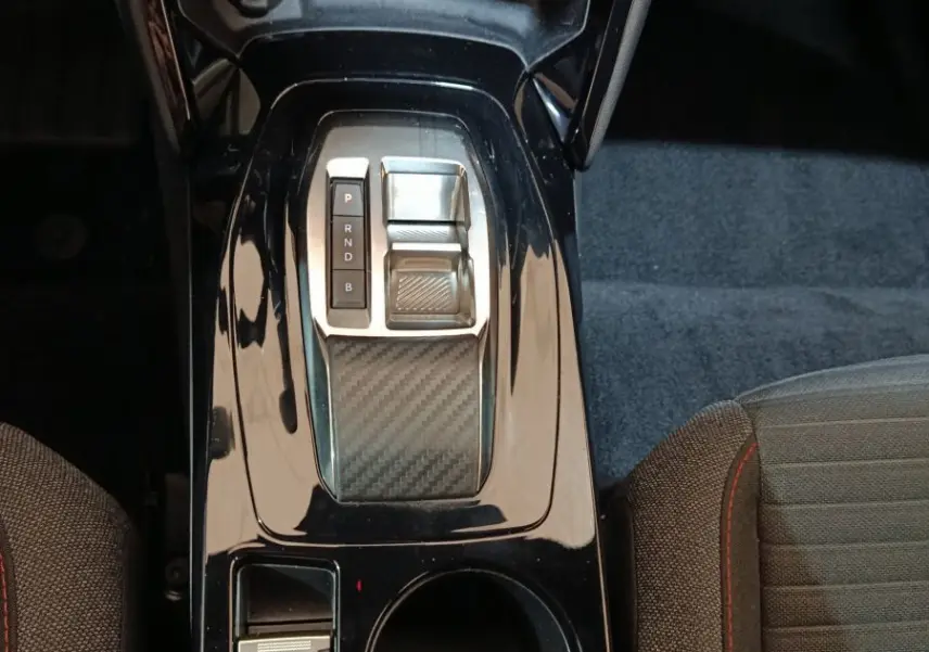 Vue plongeante sur la console centrale noire brillante du Peugeot E-2008 électrique avec sélecteur de vitesse et porte-gobelets.