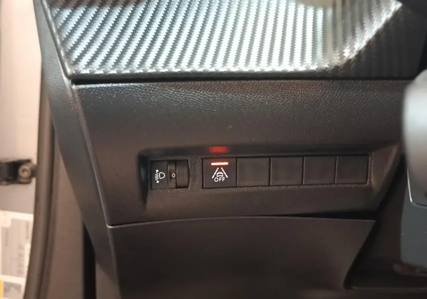 Détail du tableau de bord côté gauche avec bouton d'assistance à la conduite activé sur Peugeot E-2008 gris clair électrique.