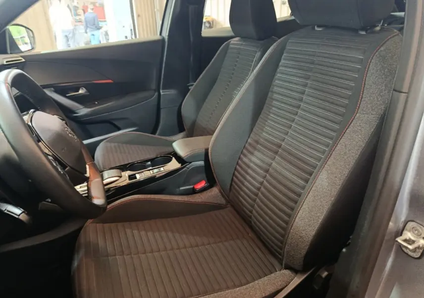 Vue intérieure côté conducteur du Peugeot E-2008 électrique gris clair, montrant les sièges avant en tissu avec surpiqûres rouges.
