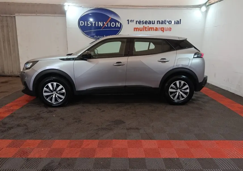Profil côté gauche d'un Peugeot E-2008 électrique gris clair 2023, dans un showroom avec sol à damiers noir et rouge.