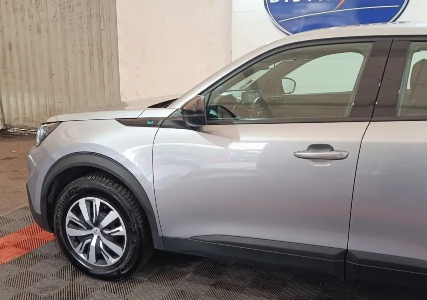 Vue de profil côté gauche du Peugeot E-2008 électrique gris clair, mettant en valeur la jante et le badge "e" près de l'aile avant.