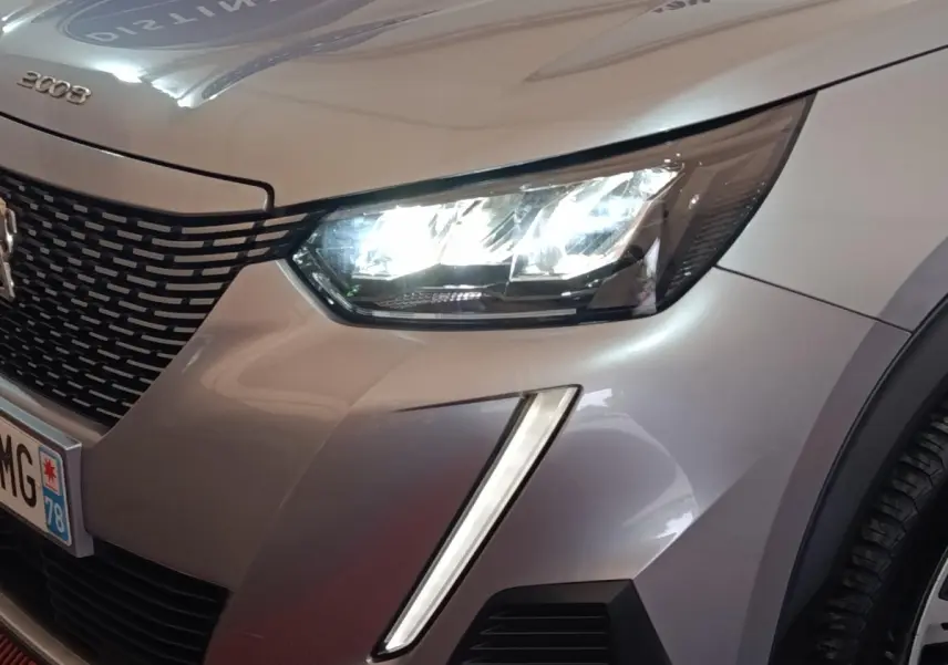Gros plan sur l'avant droit gris clair du Peugeot E-2008 électrique 2023, avec phare LED allumé et calandre noire.