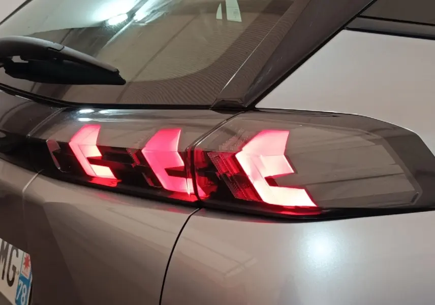 Gros plan sur le feu arrière droit rouge allumé du Peugeot E-2008 électrique gris clair 2023.