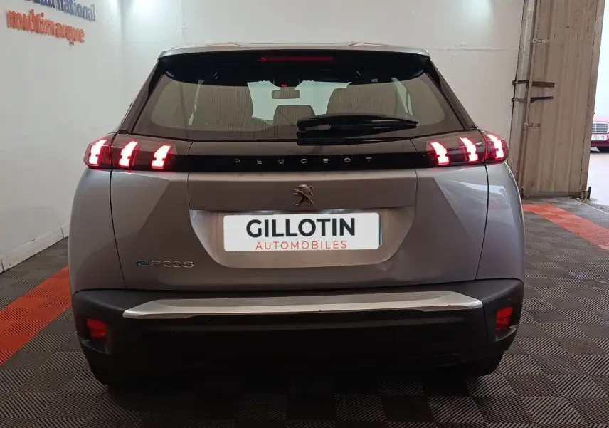 Vue arrière d’un Peugeot E-2008 électrique gris clair avec feux LED allumés en intérieur showroom.