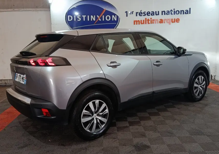 Peugeot E-2008 électrique gris clair vue 3/4 arrière droit, feux LED et jantes alliage distinctives visibles.