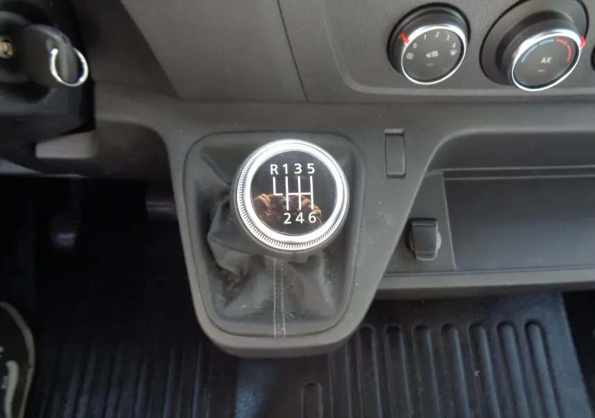 Gros plan sur le levier de vitesses manuel du fourgon Opel Movano blanc polaire, avec commandes de climatisation visibles.