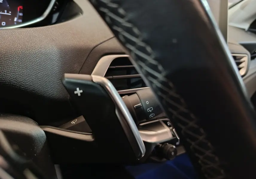 Détail du volant cuir avec palettes de changement de vitesse et commandes du Peugeot 3008 Puretech blanc, vue intérieure côté conducteur.