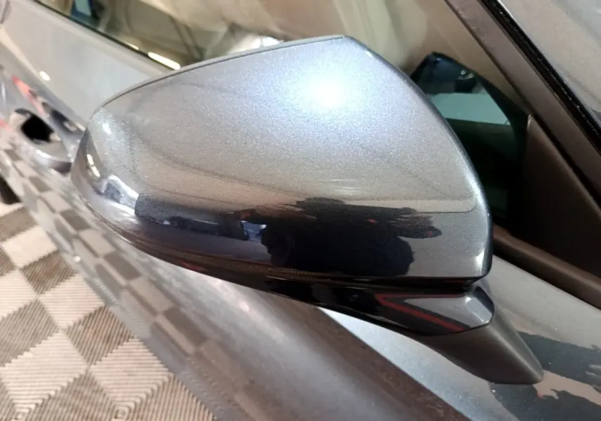 Gros plan sur le rétroviseur droit gris clair métallisé du SEAT LEON 2023, reflétant l'intérieur d'un garage.