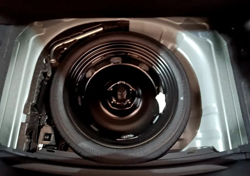 Vue plongeante sur la roue de secours galette noire dans le coffre gris clair de la SEAT LEON 2023.