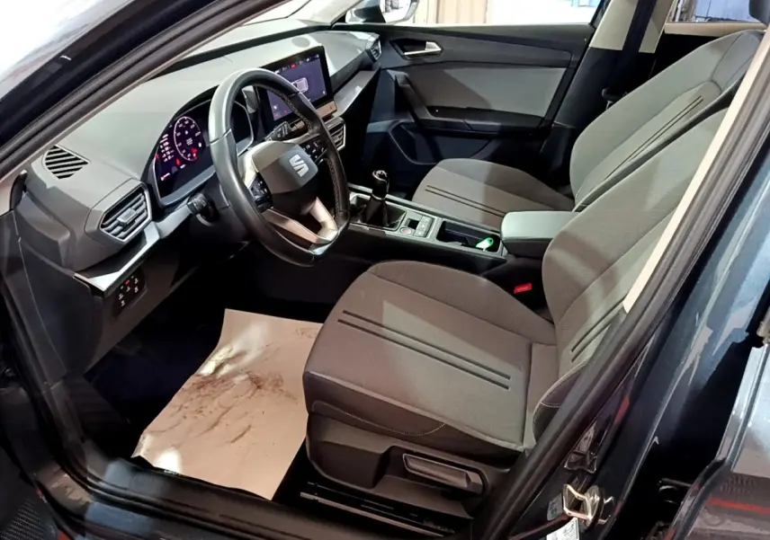 Intérieur de la SEAT Leon 2023 vu côté conducteur, sièges gris, volant cuir, écran tactile et boîte manuelle.