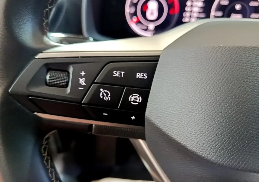 Gros plan sur les commandes à gauche du volant noir d’un SEAT Leon gris clair, avec boutons de régulateur et volume.