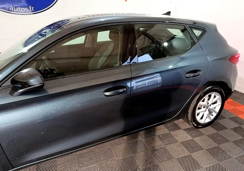 Vue latérale droite d'une SEAT Leon gris clair 2023 avec jantes alliage et rétroviseurs noirs brillants.