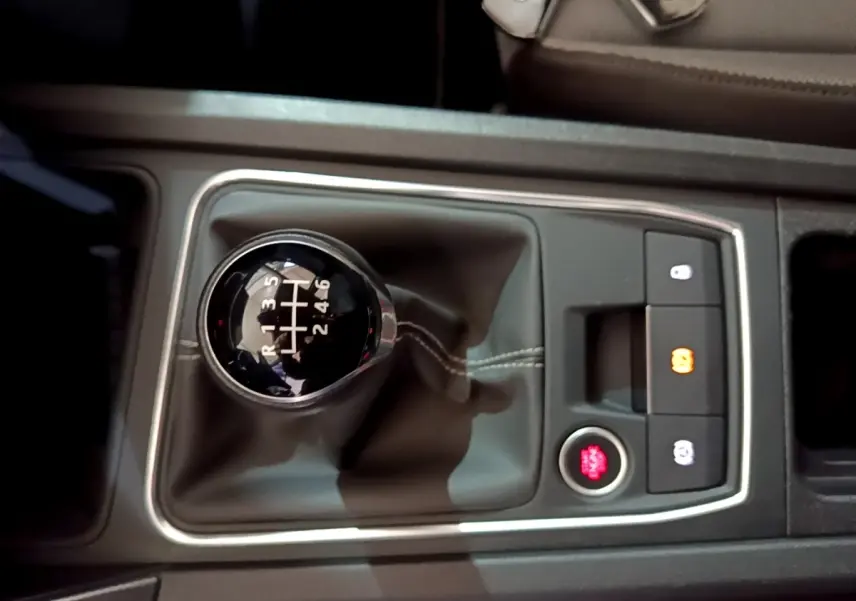 Gros plan sur la commande de boîte manuelle noire avec coutures blanches dans le console centrale d’une SEAT Leon gris clair.