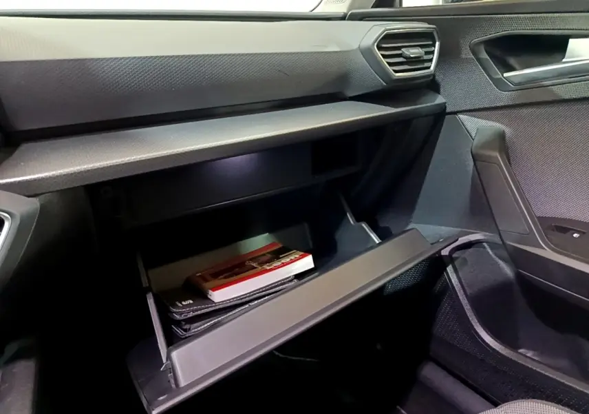 Gros plan sur la boîte à gants ouverte côté passager du SEAT Leon 2023, intérieur noir avec textures modernes.