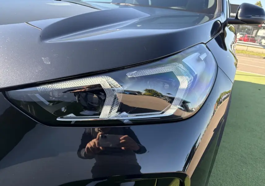 Gros plan sur le phare avant droit d’un BMW X1 noir saphir, mettant en valeur la finition LED et la carrosserie brillante.
