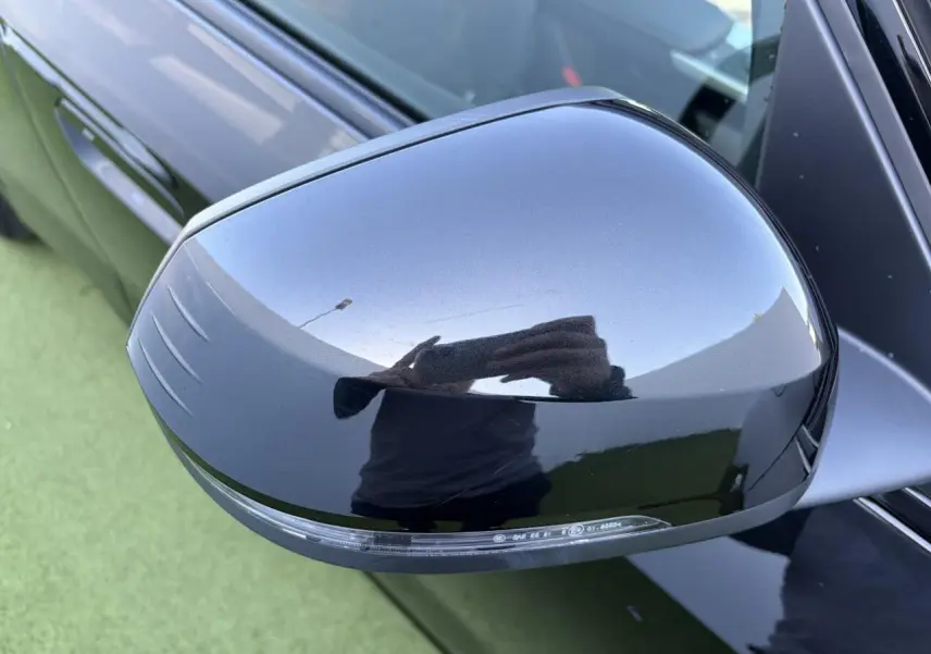 Rétroviseur extérieur droit noir saphir brillant d'une BMW X1 2025, vue rapprochée sur fond vert.