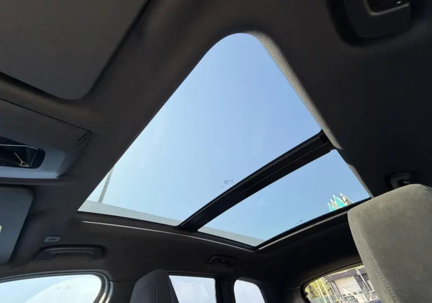 Vue intérieure du toit ouvrant panoramique en verre du BMW X1 noir Saphir, avec ciel bleu visible à travers.