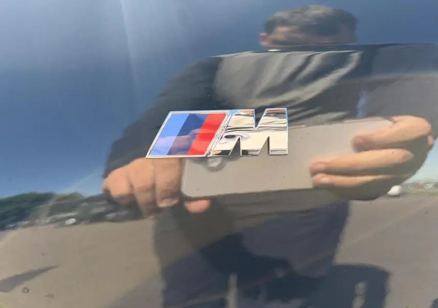 Gros plan sur l'emblème M chromé sur la carrosserie noir saphir brillante d'un BMW X1 2025.