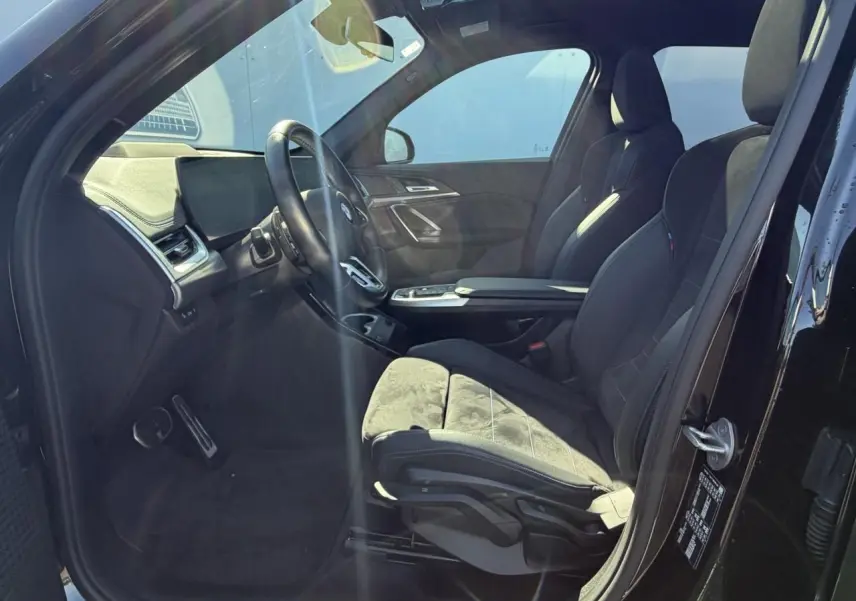 Intérieur côté conducteur de la BMW X1 noir saphir, sièges sport Alcantara avec surpiqûres bleues et tableau de bord moderne.