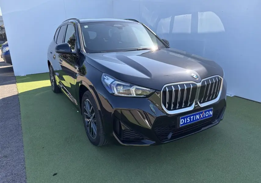 BMW X1 noir saphir vue 3/4 avant droite, avec calandre chromée et jantes alliage 18 pouces visibles.