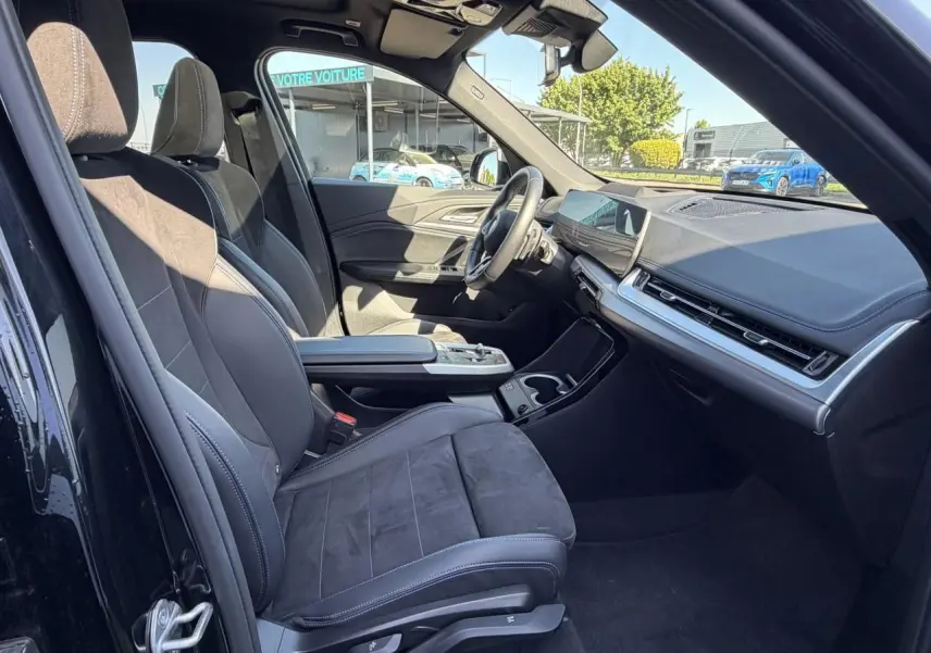 Intérieur avant droit de la BMW X1 noir saphir, sièges sport Alcantara, tableau de bord moderne avec écran tactile incurvé.