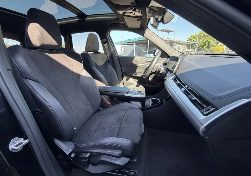 Vue intérieure côté conducteur du BMW X1 2025 avec sièges sport Alcantara noirs et toit ouvrant panoramique.
