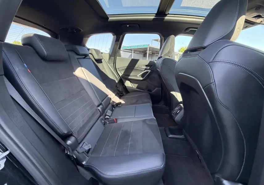 Vue intérieure arrière de la BMW X1 noire avec banquette Alcantara, toit ouvrant panoramique et finitions M Sport.