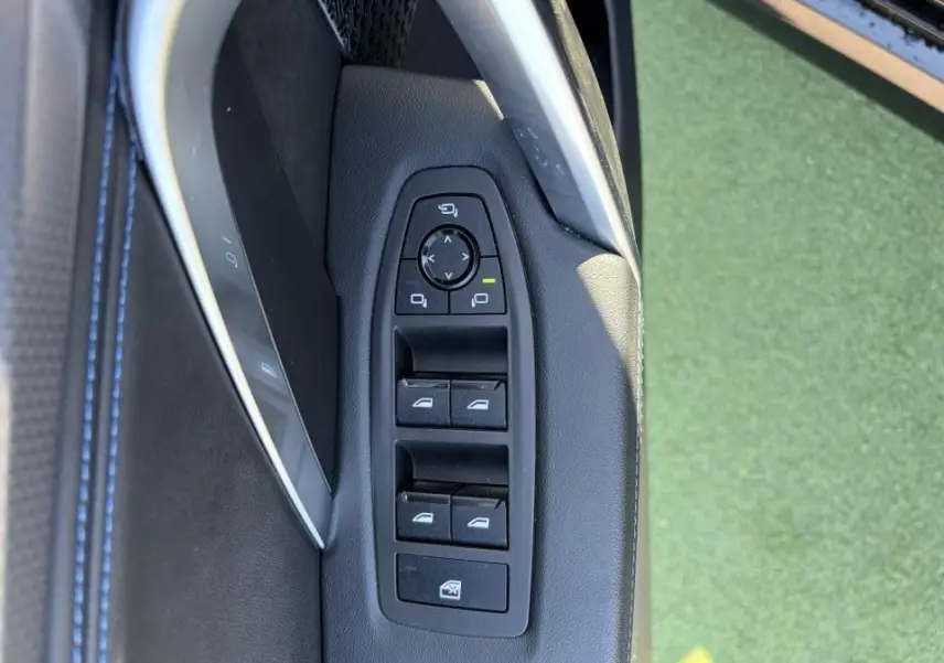 Gros plan sur les commandes de lève-vitres et rétroviseurs côté gauche, intérieur noir avec surpiqûres bleues du BMW X1 noir Saphir.