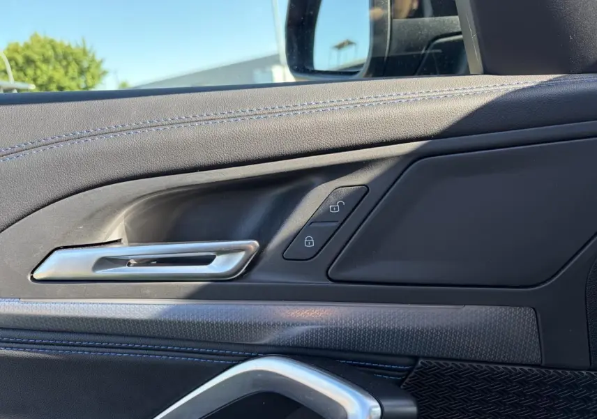 Détail de la porte côté conducteur d’un BMW X1 noir Saphir, montrant la poignée argentée et les boutons de verrouillage.