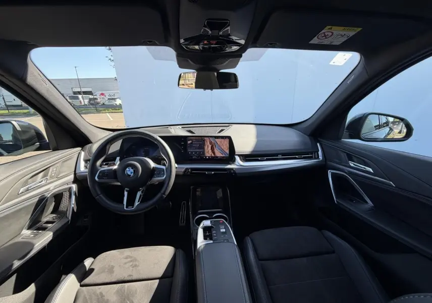 Vue intérieure avant du BMW X1 noir Saphir 2025, mettant en valeur le tableau de bord digital et le volant M cuir.
