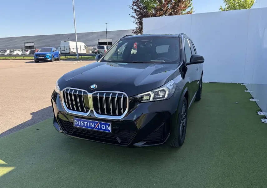 BMW X1 noir saphir vue 3/4 avant droite, calandre imposante et projecteurs LED sur parking extérieur.