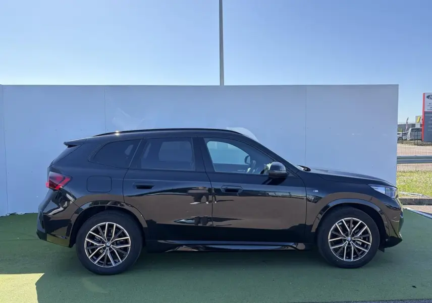 Profil droit d’un BMW X1 noir saphir 2025 avec jantes alliage 18 pouces et toit panoramique visible.