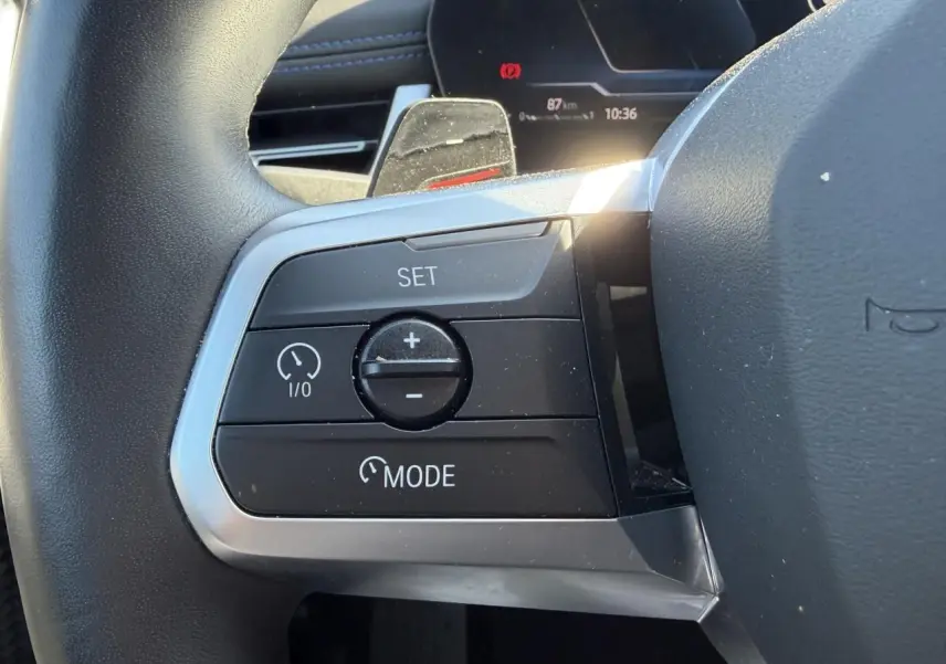 Gros plan sur les commandes de régulateur de vitesse au volant cuir du BMW X1 noir Saphir 2025.