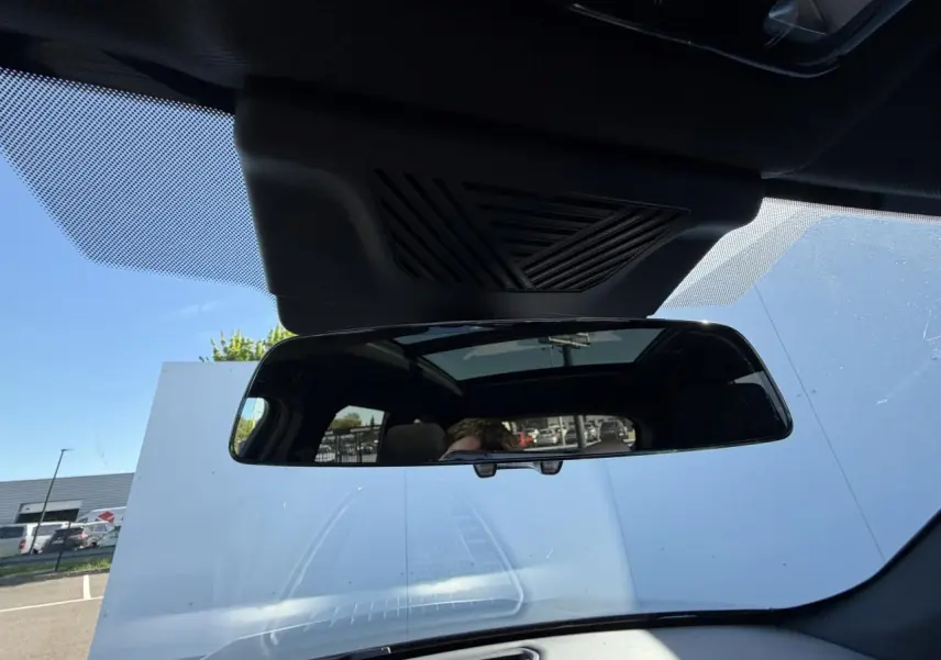 Vue intérieure centrée sur le rétroviseur intérieur et le toit ouvrant panoramique du BMW X1 noir Saphir 2025.