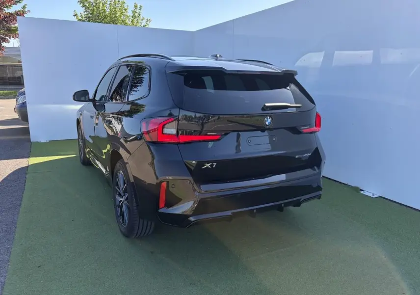 BMW X1 noir saphir vue 3/4 arrière droit, avec feux LED et vitres teintées sur fond extérieur clair.