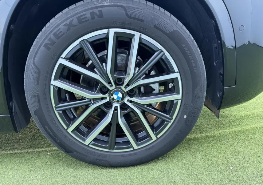 Gros plan sur la jante alliage 18 pouces bicolore du BMW X1 noir saphir, avec pneu Nexen visible sur sol vert.