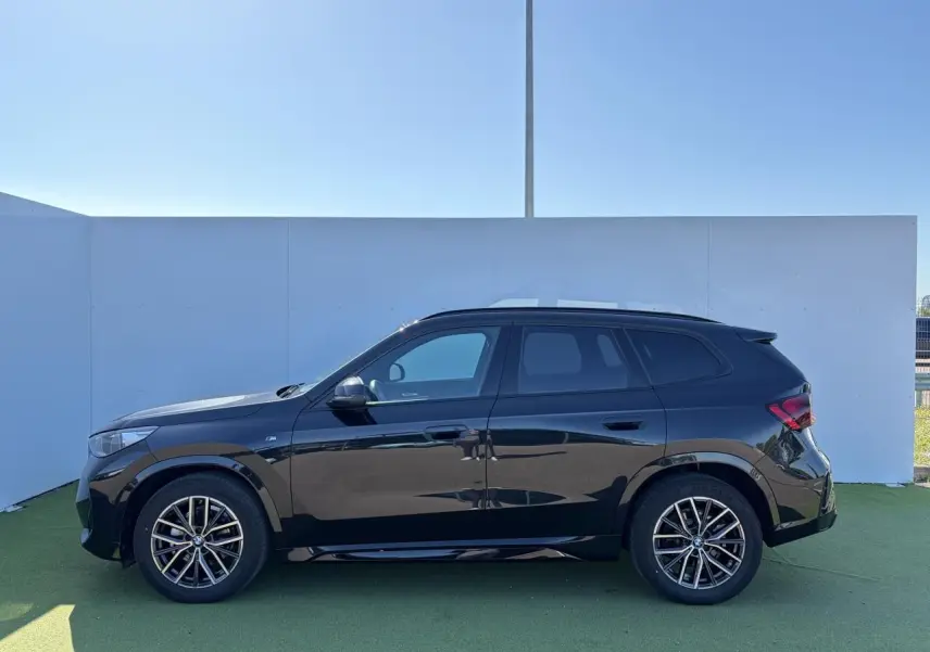 Profil côté gauche d’un BMW X1 noir saphir 2025 avec jantes alliage 18 pouces et toit panoramique visible.