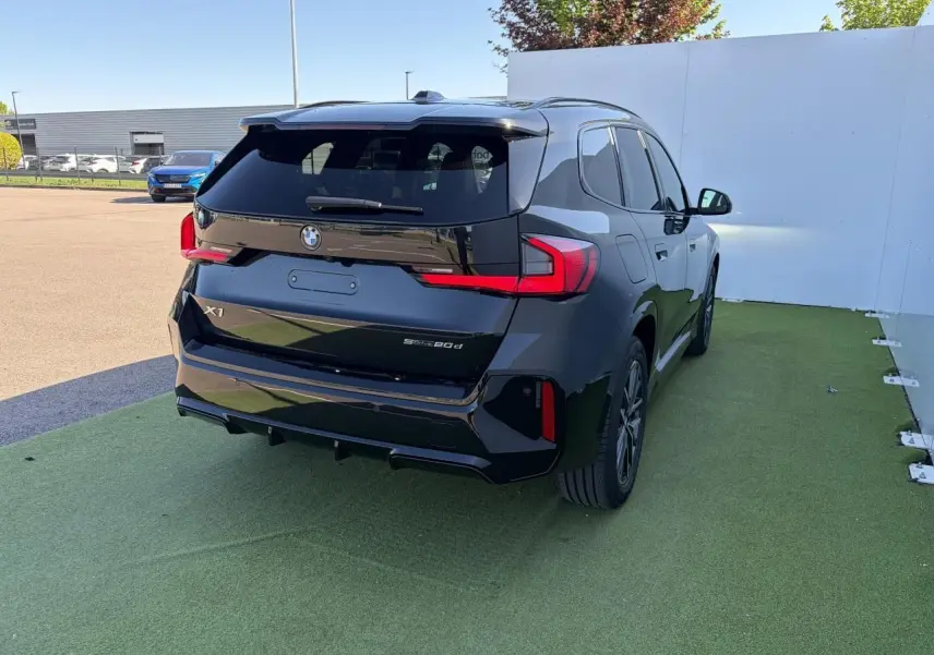 BMW X1 noir saphir vue 3/4 arrière droit, avec feux LED distinctifs et toit ouvrant panoramique visible.