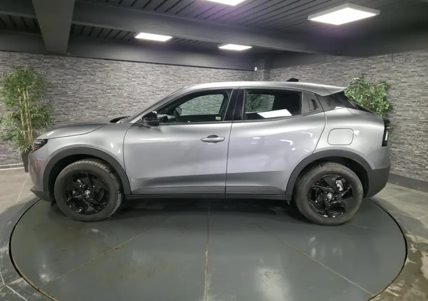 Vue de profil côté gauche d'une Alfa Romeo Junior 1.2 Ibrida gris métallisé avec jantes alliage noires dans un showroom.