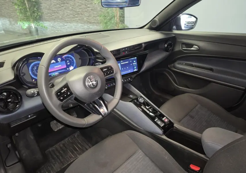 Vue intérieure côté conducteur de l'Alfa Romeo Junior 1.2 hybride 2025, avec tableau de bord digital et sellerie noire.