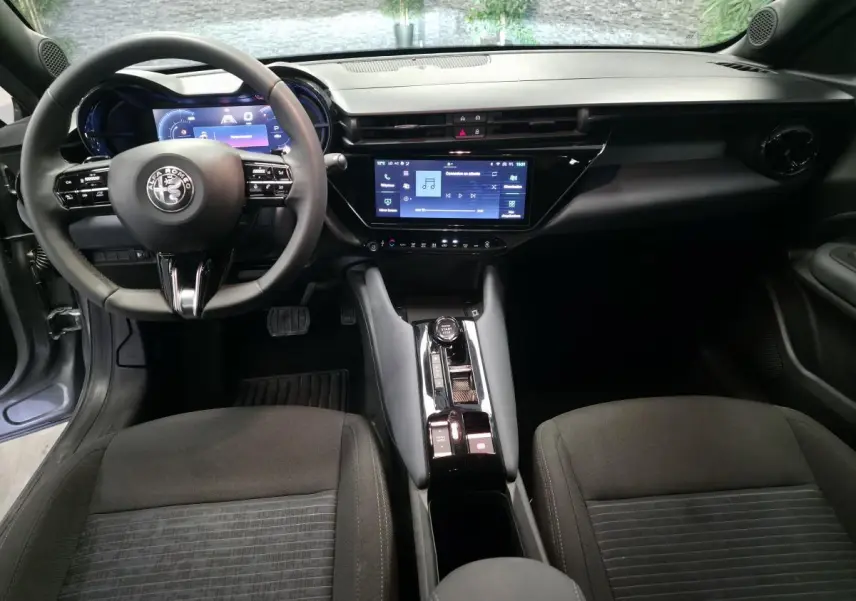 Vue intérieure avant de l'Alfa Romeo Junior 1.2 Ibrida 2025, tableau de bord moderne avec écran tactile et volant multifonctions.