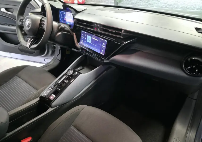Intérieur de l'Alfa Romeo Junior 1.2 Ibrida 2025 vu côté conducteur, tableau de bord moderne avec écran tactile.